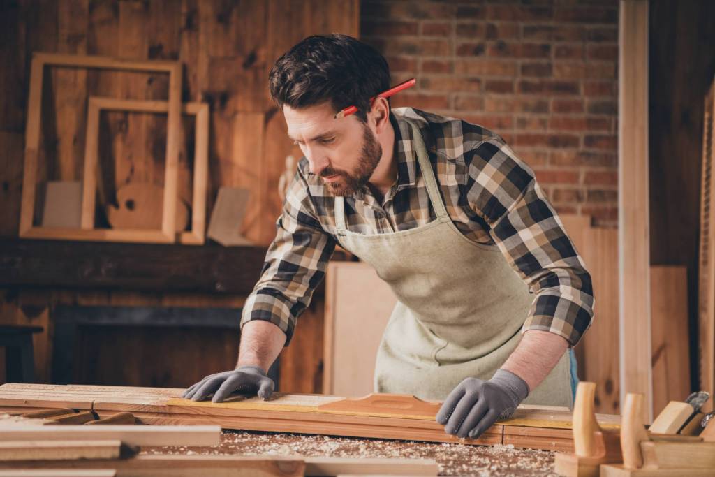 Menuisier avec un crayon sur l'oreille en train d'assembler des morceaux de bois
