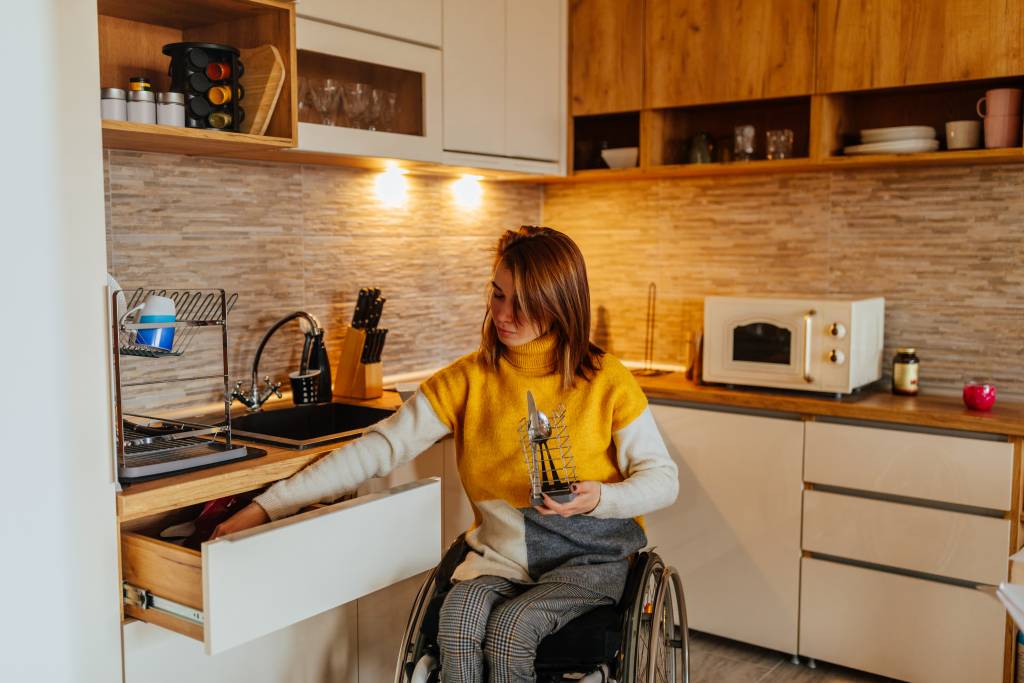 Photo d'une femme en fauteuil roulant cherchant des couverts dans le tiroir d'une cuisine